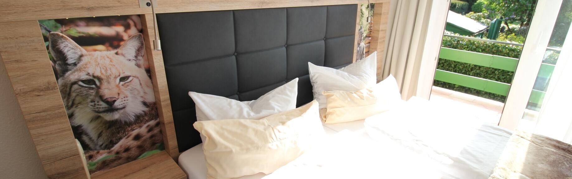 Unsere Junior Suite mit Balkon. Hier sind gemütliche Bett mit große Kissen und schöne Bild.